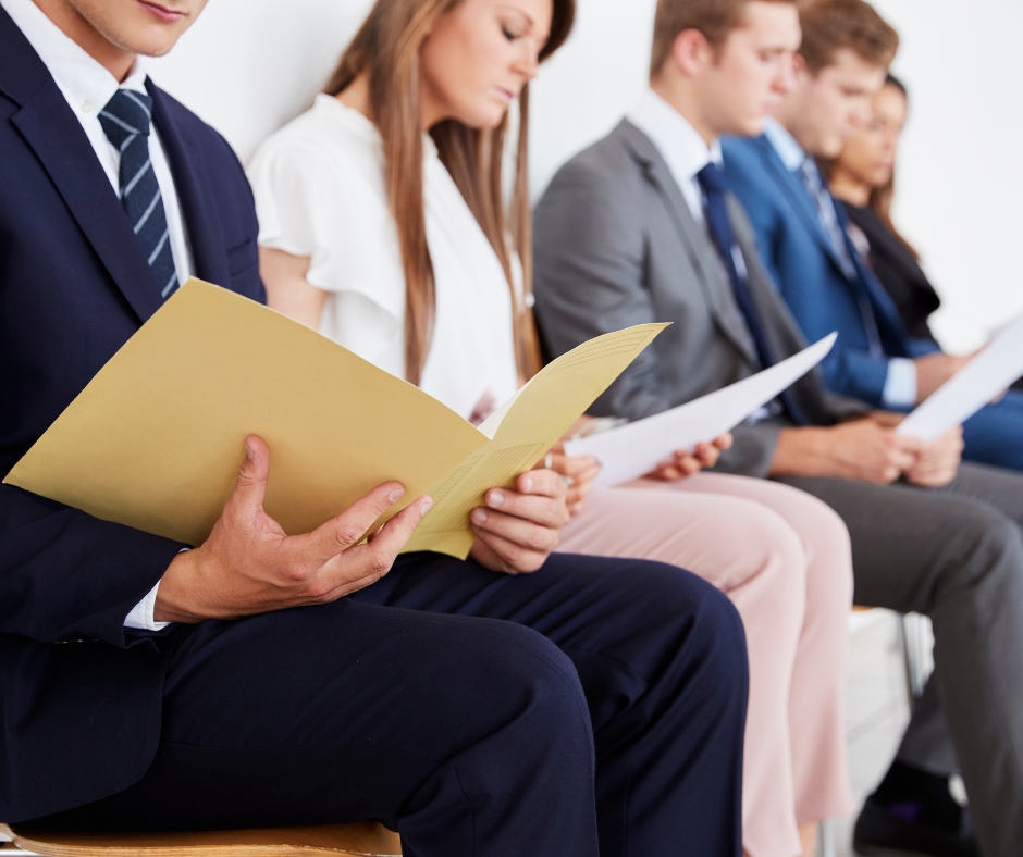 a slate of job interview applicants sitting on que with a strong emphasis on what they are wearing as a depiction of the blog Rethinking What It Means to Dress for an Interview